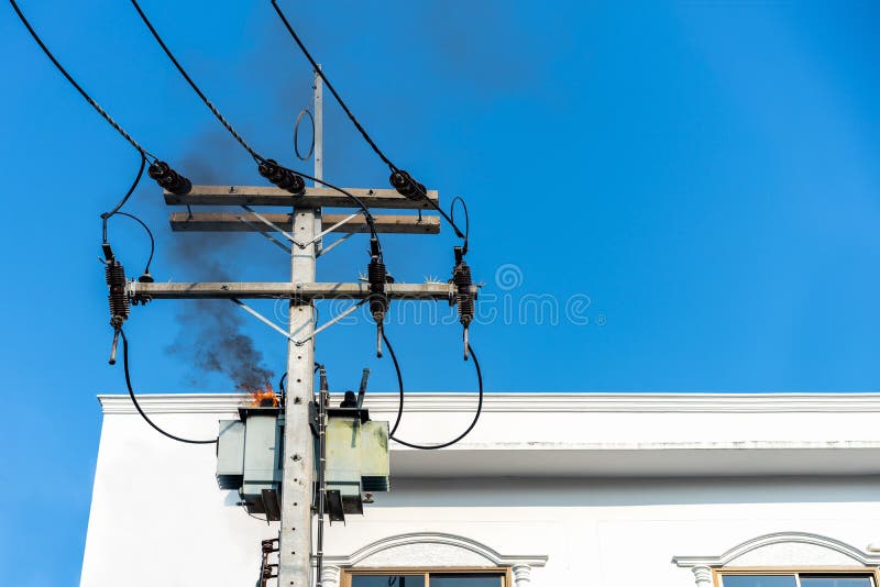 Energiepylonüberlastung oder elektrischer Kurzschluss am Transformator auf Pfosten und Feuer oder Flamme mit Rauche auf blauem Hi