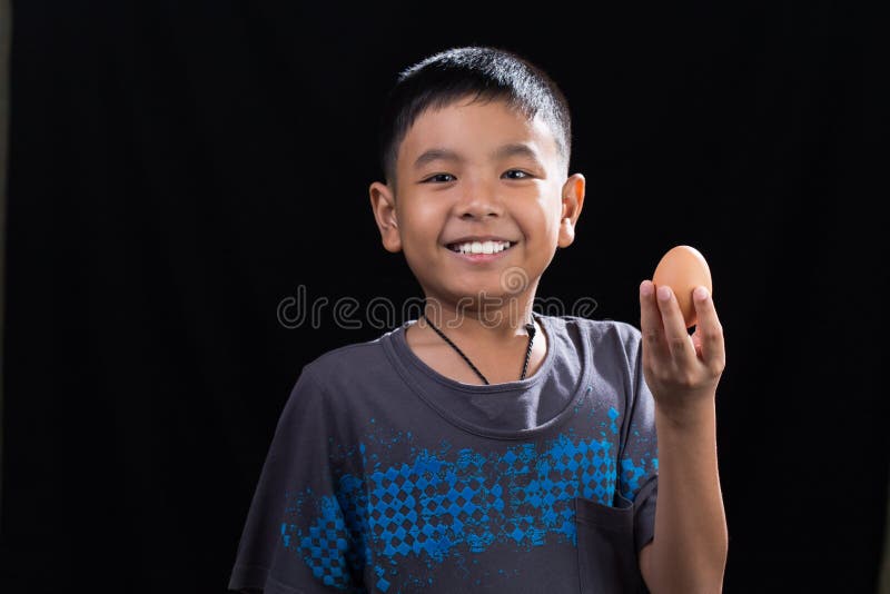 Enfant asiatique tenant l'oeuf dans sa main sur le fond noir photographie stock Enfant asiatique tenant l'oeuf dans sa main sur le fond noir photographie stock