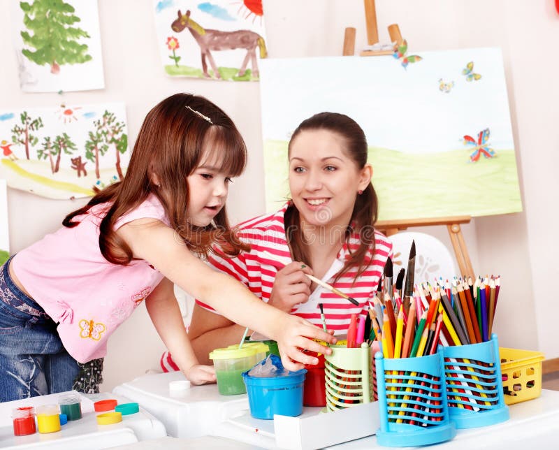 Enfant avec des peintures d'attraction de professeur dans la chambre de pièce. photo stock Enfant avec des peintures d'attraction de professeur dans la chambre de pièce. photo stock