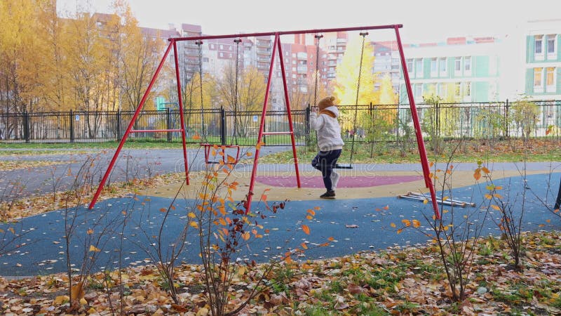 Enfant balançant sur balançoire dans l'aire de jeux avec béquilles en automne. la fille a une jambe cassée. banque de vidéos