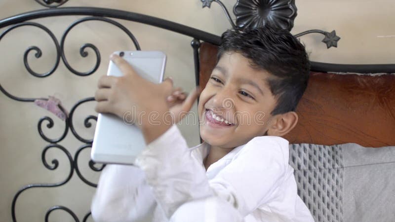 Enfant caucasien asiatique de garçon de petit Indien adorable mignon prenant les selfies drôles sur le téléphone portable ou la c banque de vidéos