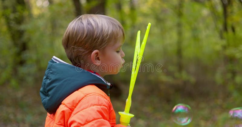 Enfant caucasien heureux jouant avec des bulles de savon dans un parc d'automne. clips vidéos