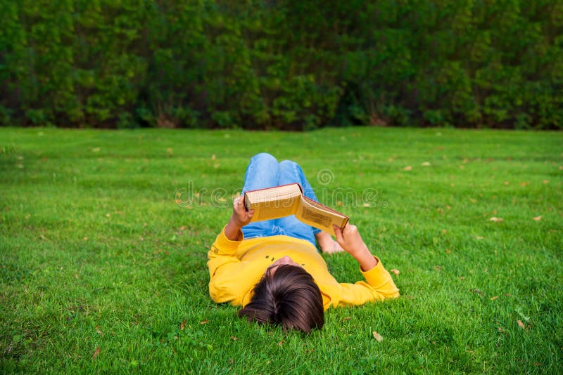 Enfant caucasien look décontracté en jean bleu et hoodie jaune pondre sur herbe verte profiter lire des histoires amusantes dans l images libres de droits