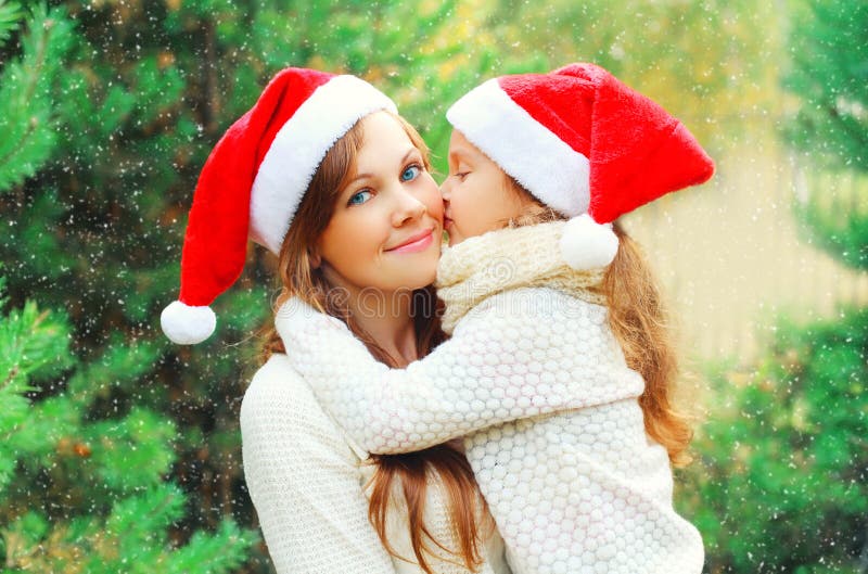 Enfant de famille de Noël embrassant la mère dans des chapeaux rouges de Santa ensemble au-dessus de l'arbre photographie stock libre de droits Enfant de famille de Noël embrassant la mère dans des chapeaux rouges de Santa ensemble au-dessus de l'arbre photographie stock libre de droits