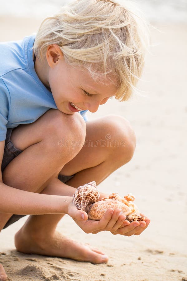 Enfant heureux à la plage rassemblant des coquilles de mer photo stock Enfant heureux à la plage rassemblant des coquilles de mer photo stock