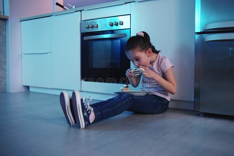 Enfant mangeant du gâteau la nuit près du réfrigérateur