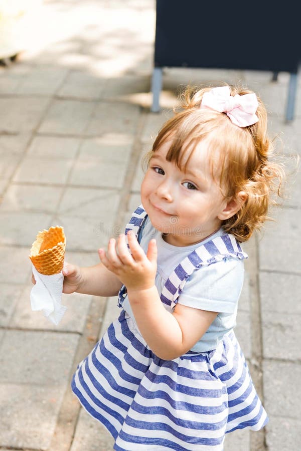 Enfant mangeant la crème glacée près du café Enfant bouclé de Funy avec la glace extérieure en parc images stock Enfant mangeant la crème glacée près du café Enfant bouclé de Funy avec la glace extérieure en parc images stock