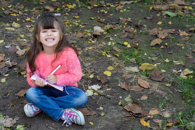 Enfant mignon étonné dans des lunettes, écrivant dans le carnet utilisant le crayon, souriant photographie stock Enfant mignon étonné dans des lunettes, écrivant dans le carnet utilisant le crayon, souriant photographie stock