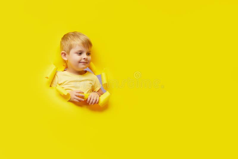 Enfant piaulant paraissant peu surpris par le trou de papier jaune vif. Annoncez les biens des enfants. Concept heureux d'enfance. photographie stock