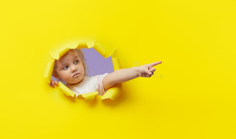 Enfant piaulant paraissant peu surpris par le trou de papier jaune vif. Représentation de la main pour me ranger du côté. Annoncez image stock