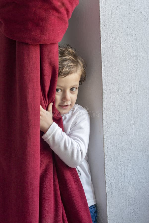 Child hiding behind a red curtain with smiling gesture. Child hiding behind a red curtain with smiling gesture