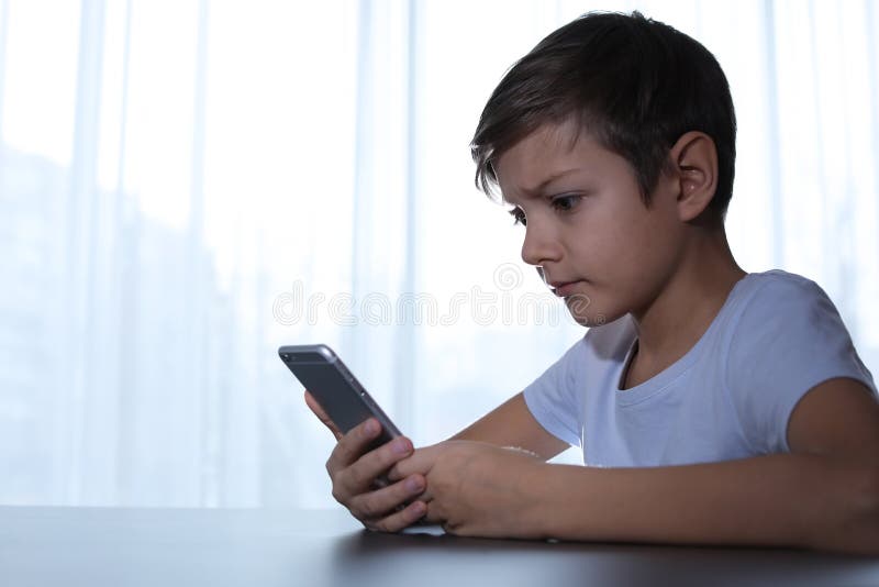 Enfant terrifié avec le smartphone à la table à l'intérieur image libre de droits Enfant terrifié avec le smartphone à la table à l'intérieur image libre de droits