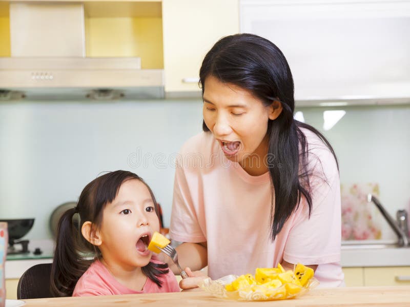Enfantez la fille de alimentation mangeant des fruits dans la cuisine photo stock Enfantez la fille de alimentation mangeant des fruits dans la cuisine photo stock