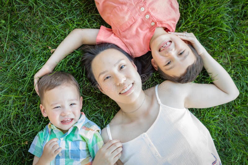 Enfants chinois de mère et de métis s'étendant sur l'herbe photo stock Enfants chinois de mère et de métis s'étendant sur l'herbe photo stock