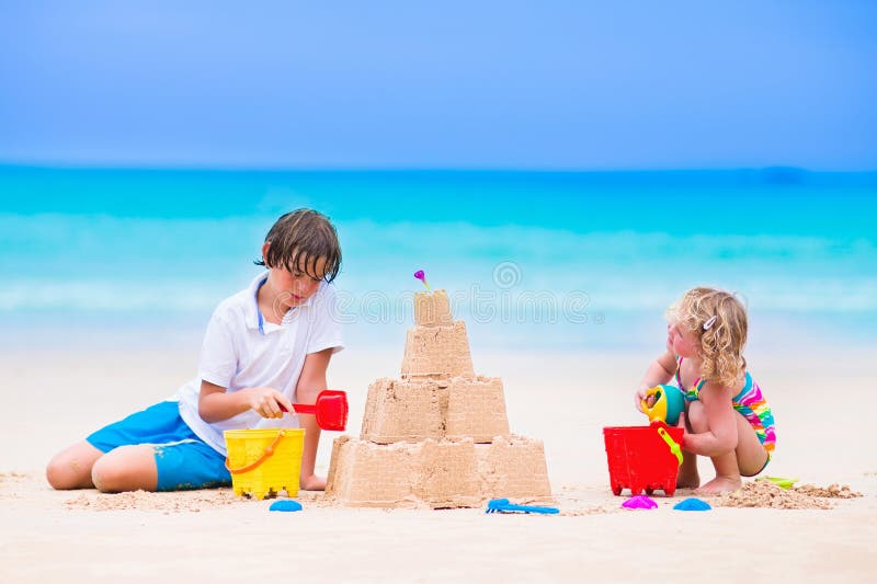 Kids playing on a beach. Two children build a sand castle at the sea shore. Family vacation on a tropical island. Boy and girl digging with toy spade and kid spade. Traveling with young child. Kids playing on a beach. Two children build a sand castle at the sea shore. Family vacation on a tropical island. Boy and girl digging with toy spade and kid spade. Traveling with young child.