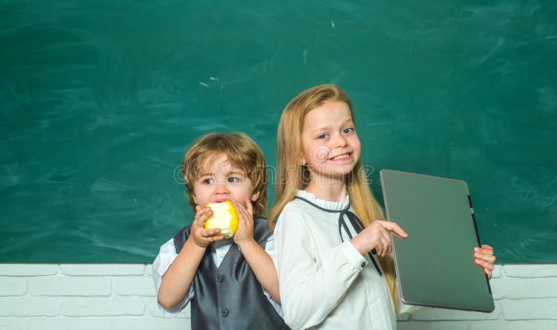 Enfants d'?cole contre le tableau vert Fille et garçon avec l'expression heureuse de visage près du bureau avec des fournitures s images stock Enfants d'?cole contre le tableau vert Fille et garçon avec l'expression heureuse de visage près du bureau avec des fournitures s images stock