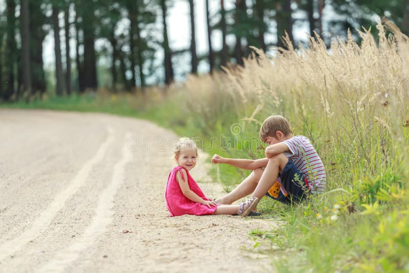 Enfants d'enfant de mêmes parents jouant en poussière se reposant sur le chemin de terre d'été photos libres de droits Enfants d'enfant de mêmes parents jouant en poussière se reposant sur le chemin de terre d'été photos libres de droits