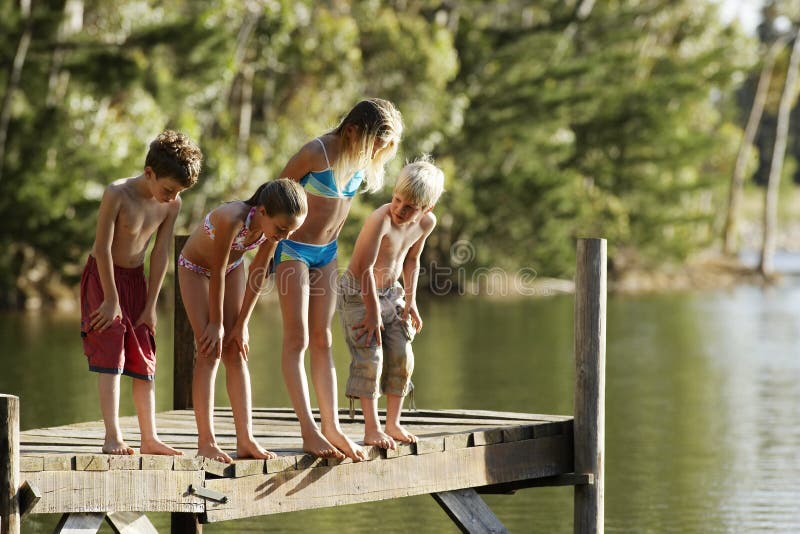 Enfants dans les vêtements de bain se tenant sur la jetée à côté du lac image stock Enfants dans les vêtements de bain se tenant sur la jetée à côté du lac image stock