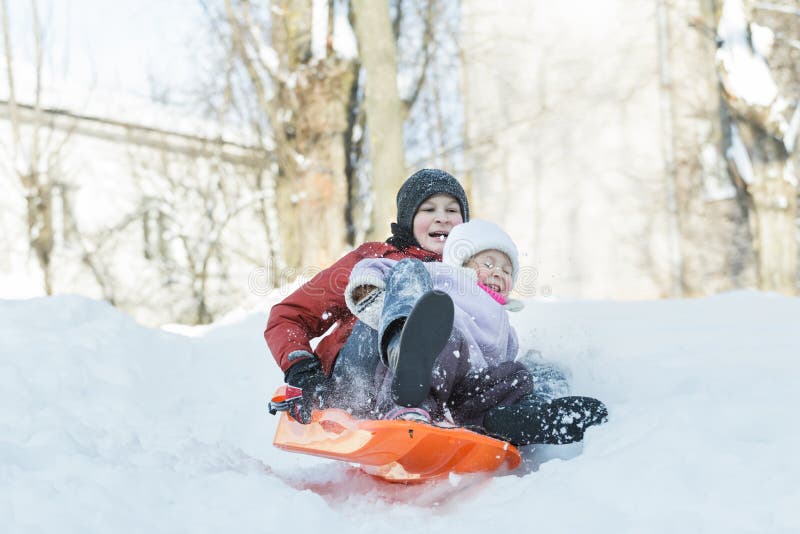 Enfants de mêmes parents ayant l'amusement incliné sur le glisseur en plastique de neige d'hiver dehors photos libres de droits Enfants de mêmes parents ayant l'amusement incliné sur le glisseur en plastique de neige d'hiver dehors photos libres de droits