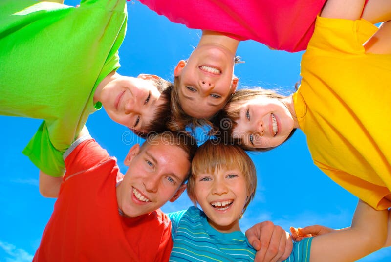 Five happy children bent over and looking downward toward the viewer, with their heads all touching in the middle. Blue sky background. Five happy children bent over and looking downward toward the viewer, with their heads all touching in the middle. Blue sky background.