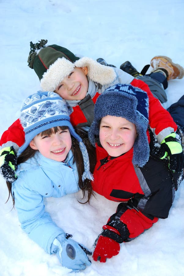 An overhead view of three siblings playing happily in the snow on a winter day. An overhead view of three siblings playing happily in the snow on a winter day.