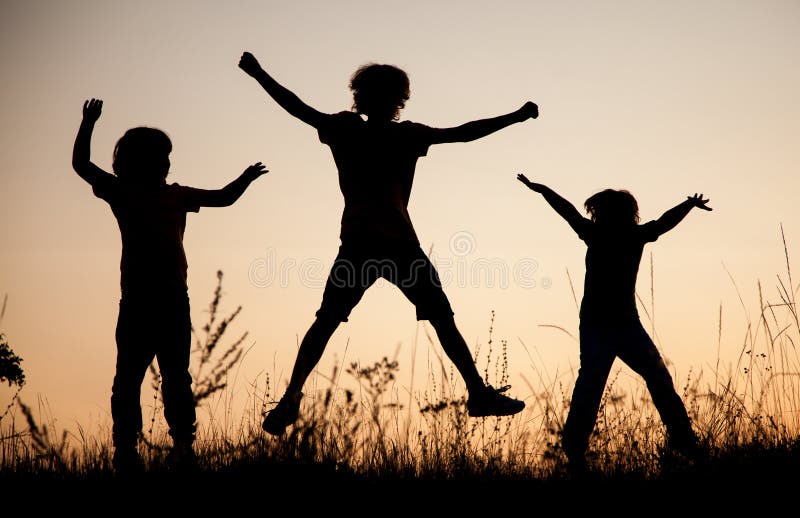 Enfants jouant sauter sur le pré de coucher du soleil d'été silhouetté images stock Enfants jouant sauter sur le pré de coucher du soleil d'été silhouetté images stock