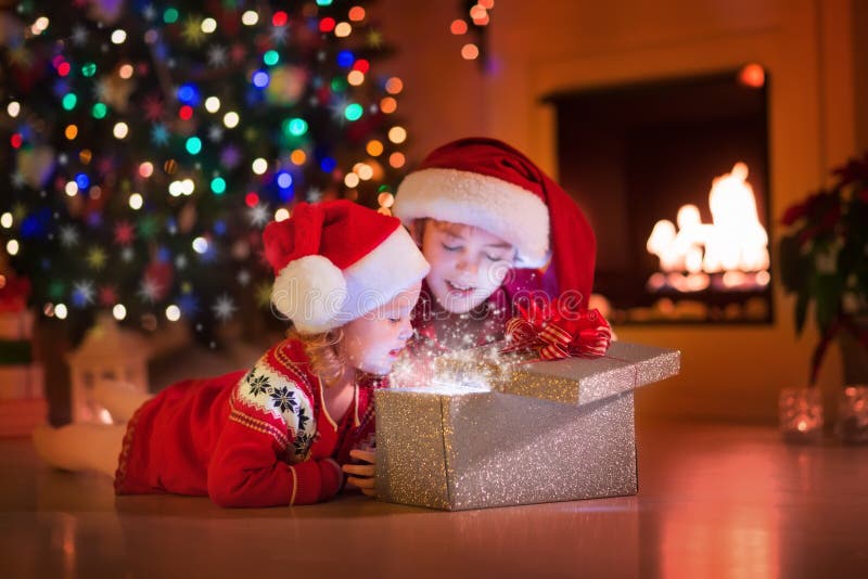 Des enfants ouvrant des cadeaux de Noël près de la cheminée photos stock