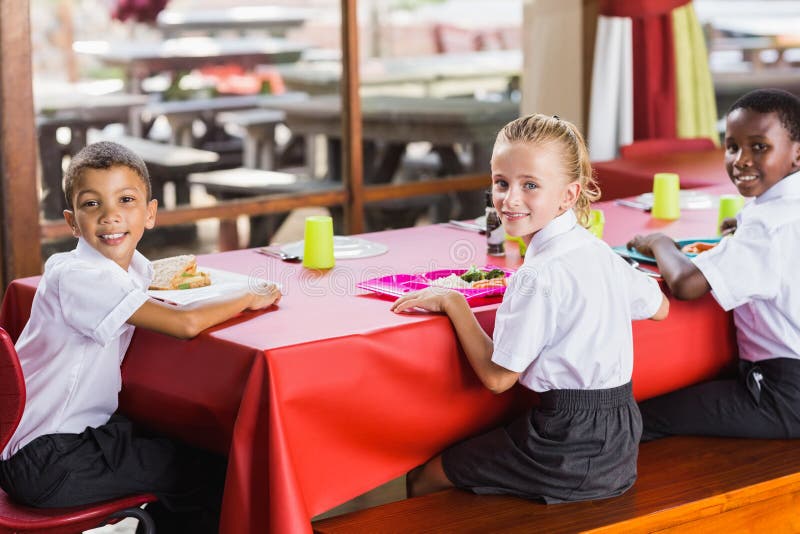 Enfants prenant le déjeuner pendant le temps de coupure dans la cafétéria de l'école images stock Enfants prenant le déjeuner pendant le temps de coupure dans la cafétéria de l'école images stock