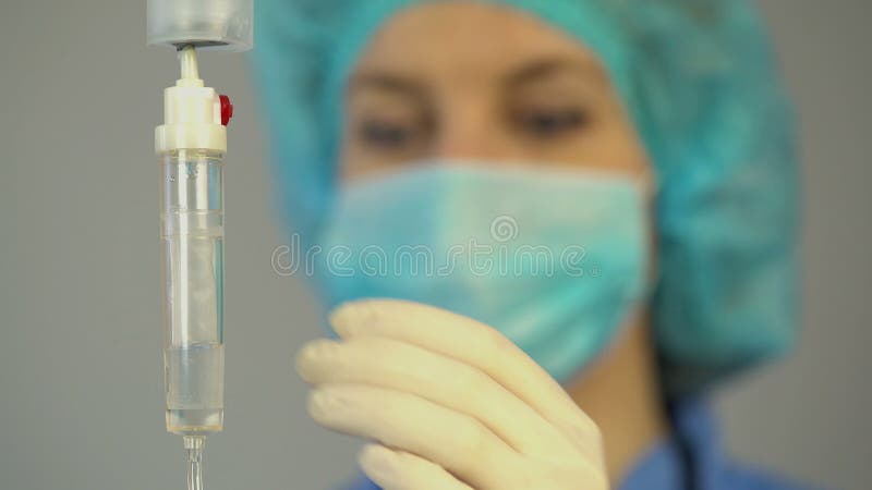 Enfermeira fêmea que verifica o conta-gotas com a medicamentação, rendendo primeiros socorros ao paciente