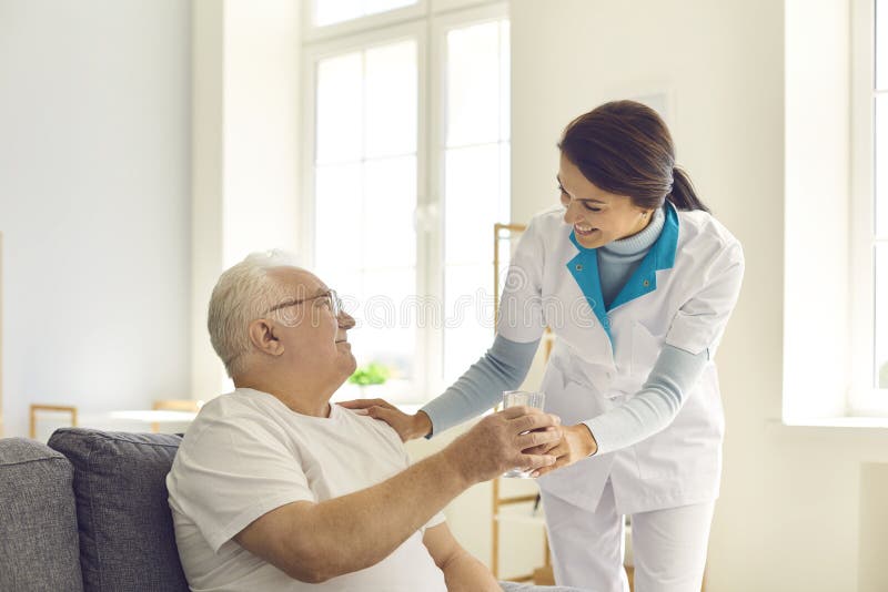 Enfermeira sorridente que dá um copo de água ao homem idoso em casa de enfermagem ou em instalação assistida