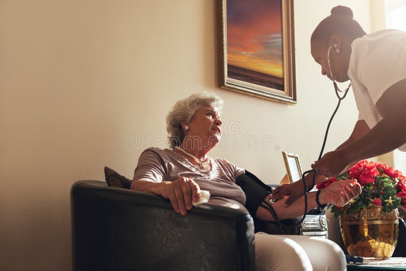 Enfermera de la atención sanitaria a domicilio que comprueba la presión arterial de la mujer mayor fotos de archivo libres de regalías Enfermera de la atención sanitaria a domicilio que comprueba la presión arterial de la mujer mayor fotos de archivo libres de regalías