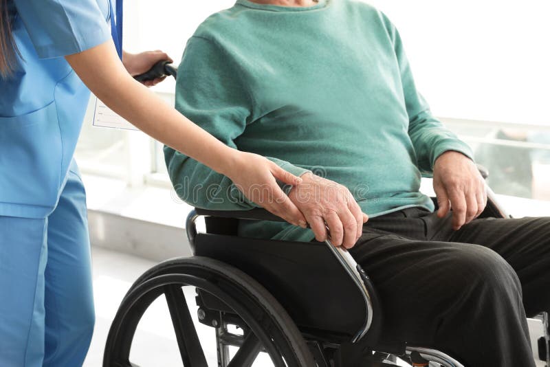 Enfermera que ayuda al hombre mayor en silla de ruedas en el hospital imagen de archivo Enfermera que ayuda al hombre mayor en silla de ruedas en el hospital imagen de archivo