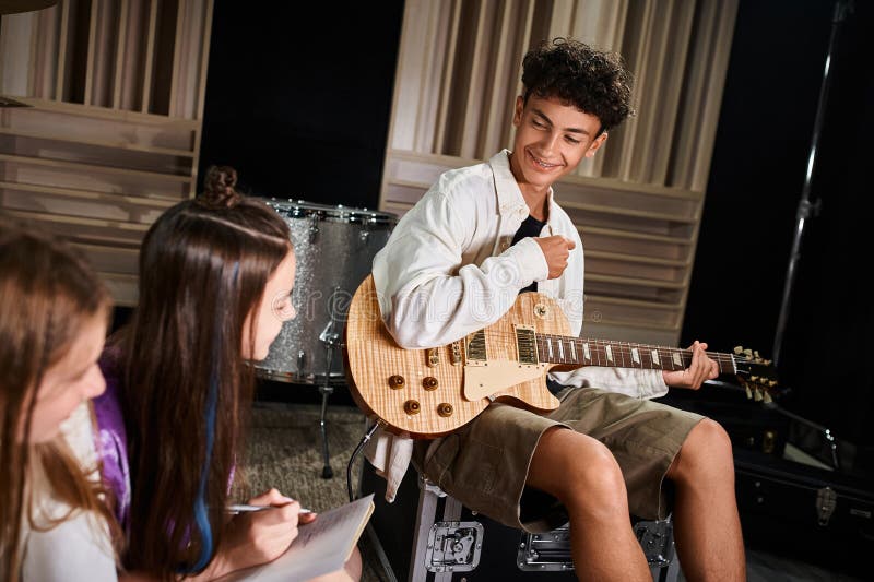 focus on joyful cute teenage boy with braces holding guitar and looking at his blurred band members, stock photo. focus on joyful cute teenage boy with braces holding guitar and looking at his blurred band members, stock photo