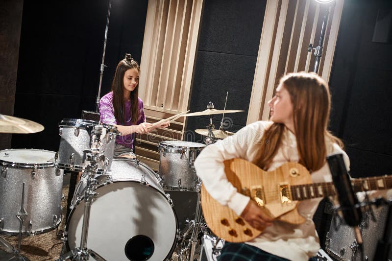 focus on pretty brunette teenage girl playing drums next to her blurred friend playing guitar, stock photo. focus on pretty brunette teenage girl playing drums next to her blurred friend playing guitar, stock photo