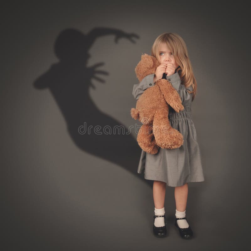 A little girl is holding a teddy bear and looking at a scary dark silhouette of an evil ghost popping out on a gray background. A little girl is holding a teddy bear and looking at a scary dark silhouette of an evil ghost popping out on a gray background.