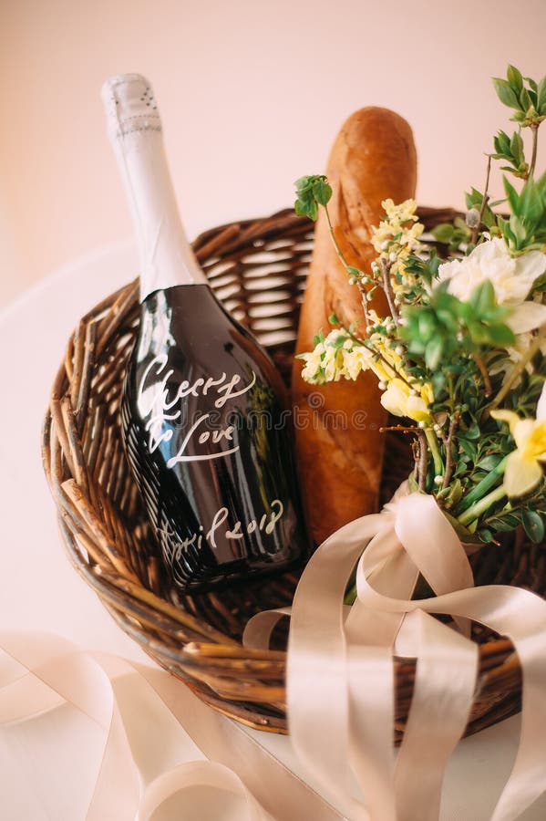 Engagement idea. Romantic picnic for two lovers. Wicker basket with two glasses of champagne with flowers, fresh baguette and a bo