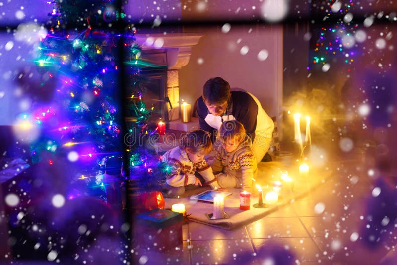 Engendrez et ses deux petits enfants s'asseyant par la cheminée de cheminée le temps de réveillon de Noël image stock Engendrez et ses deux petits enfants s'asseyant par la cheminée de cheminée le temps de réveillon de Noël image stock