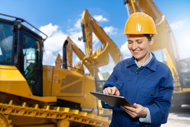 Engenheira de mulheres com capacete e tablet digital no fundo de máquinas de construção fotografia de stock royalty free