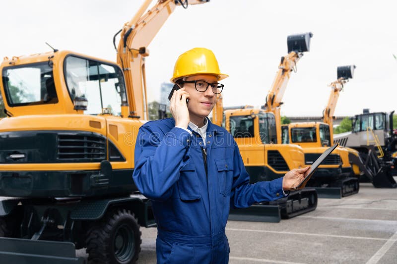 Engenheiro de capacete com smartpone e tablet digital ao lado de escavadoras de construção. imagem de stock
