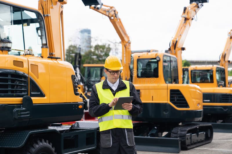 Engenheiro de capacete com tablet digital ao lado de escavadoras de construção.