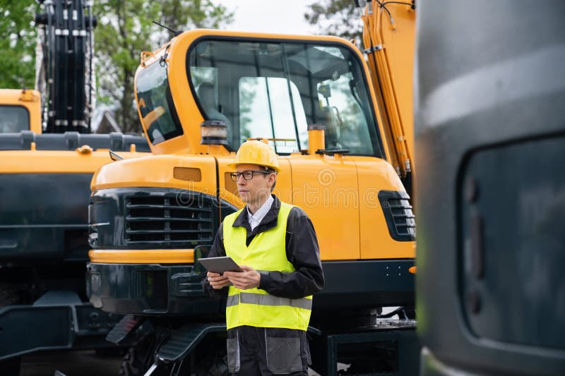 Engenheiro de capacete com tablet digital ao lado de escavadoras de construção. fotos de stock