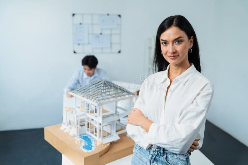 Closeup of female professional architect engineer poses with confident and looks at camera while skilled coworker focus on drawing blueprint. Creative living and design concept. Immaculate. Closeup of female professional architect engineer poses with confident and looks at camera while skilled coworker focus on drawing blueprint. Creative living and design concept. Immaculate.