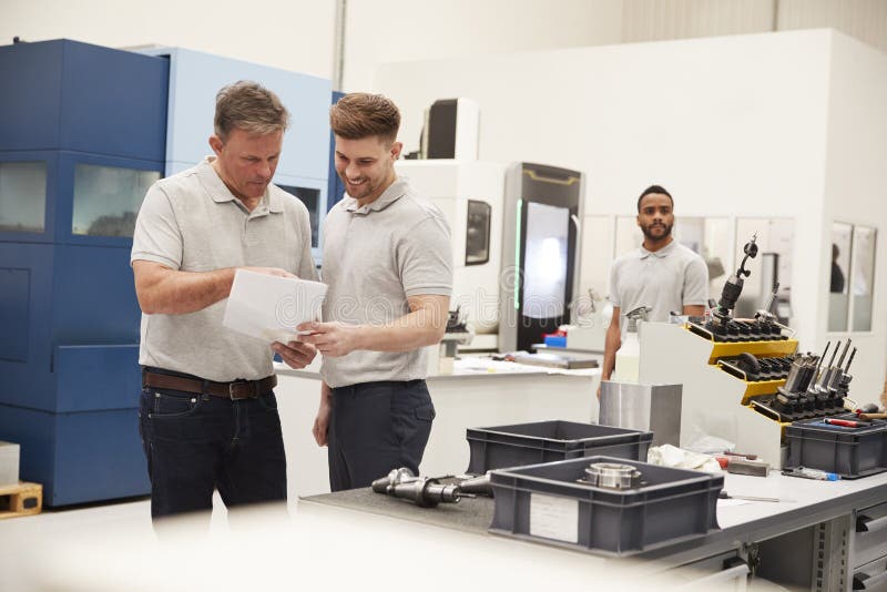 Engineer and Apprentice Meet on Floor of Engineering Workshop Stock