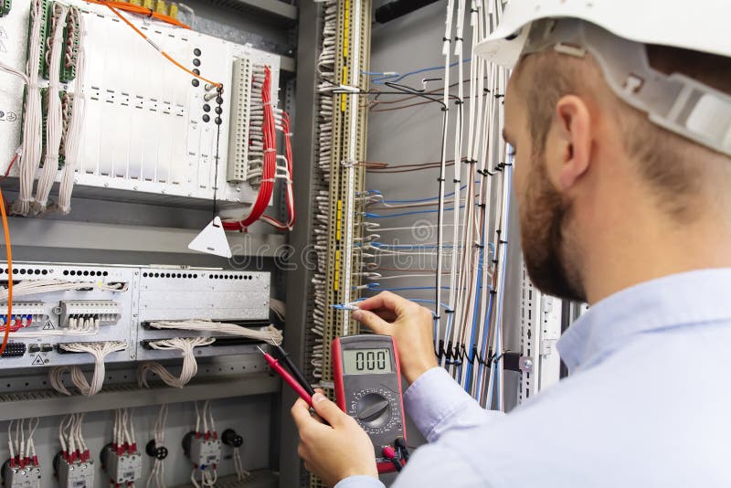 Engineer electrician with multimeter in electrical control box tests equipment. Maintenance of electrical panel stock photo