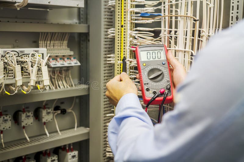 Engineer electrician with multimeter in hands at electric automation box panel. Service engineer tests circuit of industrial stock photo