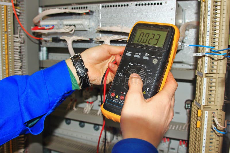 Engineer`s hands close-up with a multimeter test industrial cabinet of relay protection and automation stock photo