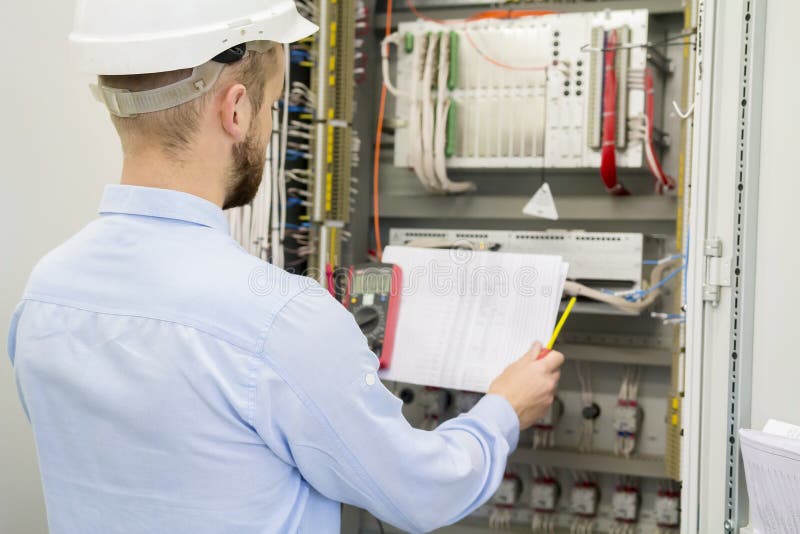 Engineer in white helmet reads design drawing against electric industrial panel. Service worker analyzes the electrical circuit stock images