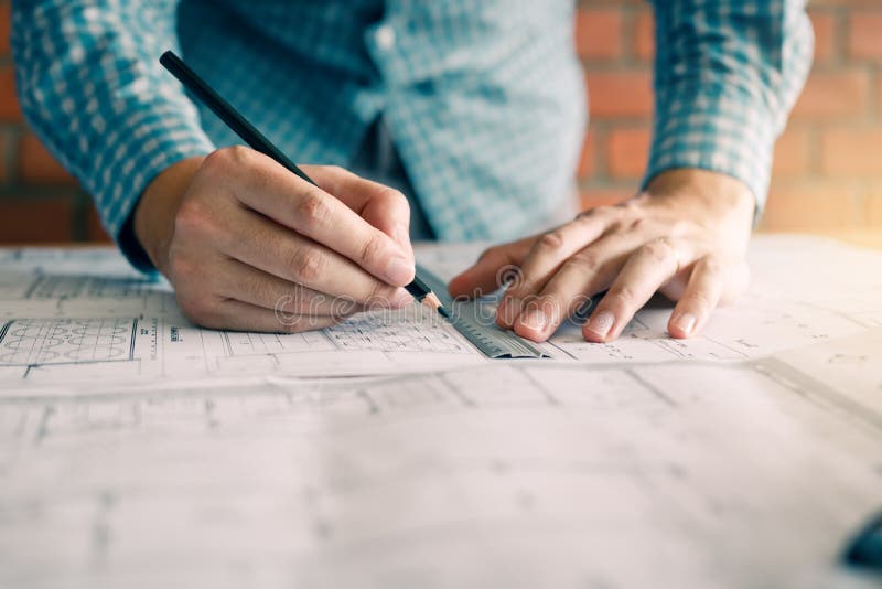 Engineering or architect reviewing blueprints and holding pencil on desk at home office stock photo