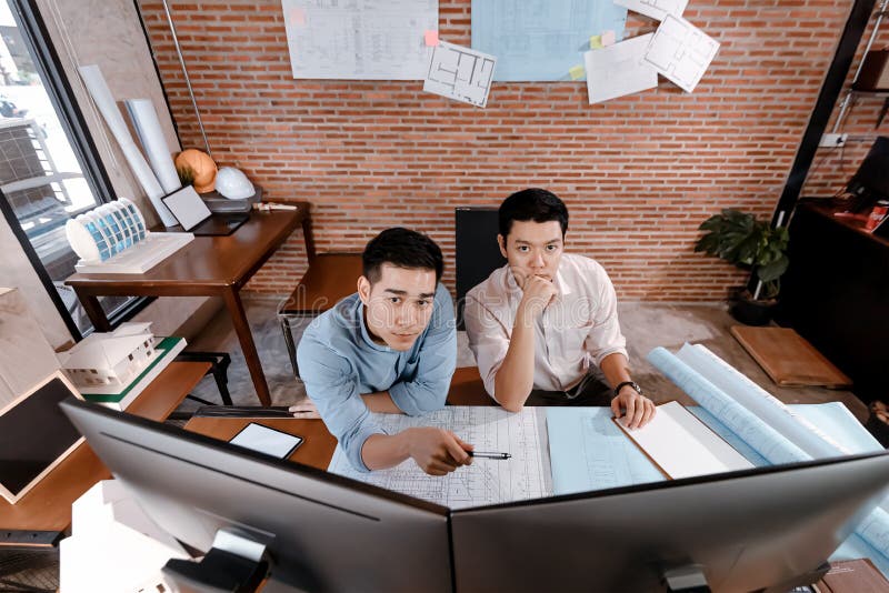 Engineers and architect reading a building and  drawing outlay construction plan as guide for builders with details on computer.