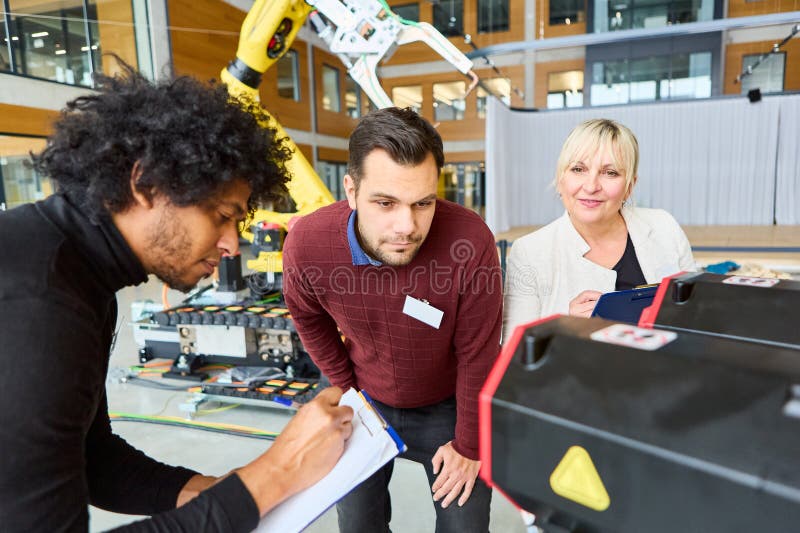 Engineers collaborating on robotics development and programming with a robotic arm in a modern facility stock photo